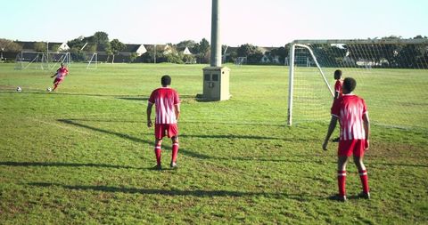 Athlete kicking soccer ball towards goal on sunny day