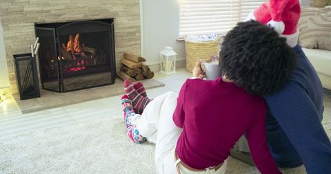 Couple relaxing by fireplace wearing santa hat and cozy socks holding mug near hearth