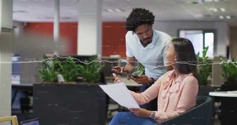 Colleagues collaborating over tablet and documents in modern office with green plants