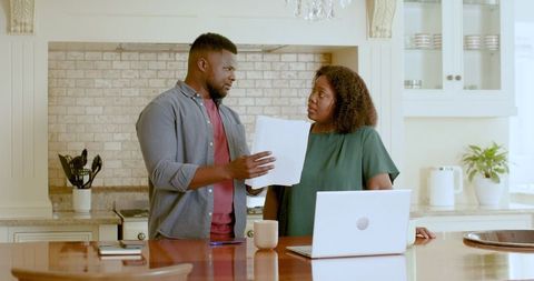 Couple discussing documents at kitchen counter with laptop