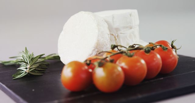 Fresh cherry tomatoes and creamy goat cheese arranged with a few sprigs of rosemary on black board. Perfect for food and health blogs, cooking magazines, and nutritional content focusing on fresh, farm-to-table ingredients.