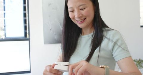 Asian woman smiling while holding compact smart gadget in bright modern home office