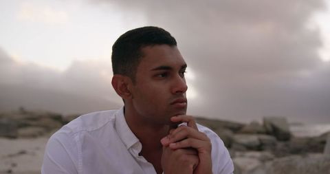 Pensive Young Man in White Shirt Contemplating on Beach at Dusk