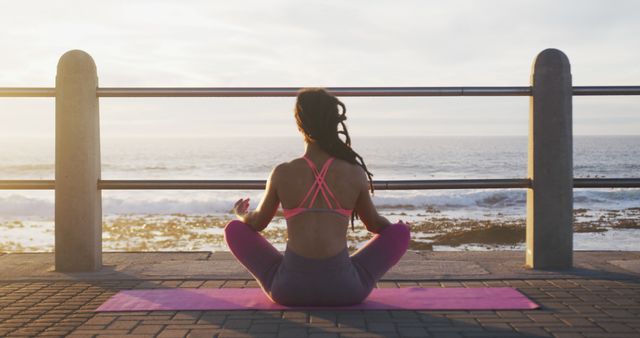 Woman practicing meditation on a yoga mat facing the ocean during sunset. Ideal for projects on mindfulness, wellness retreats, fitness programs, and content promoting relaxation and mental health. Perfect for use in advertisements for yoga classes, meditation apps, and self-care products.