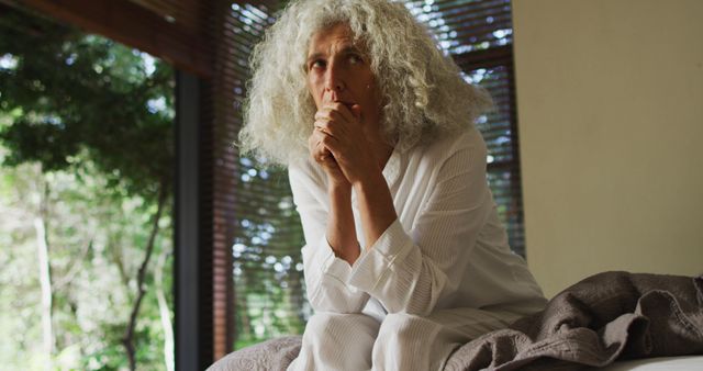 Thoughtful caucasian senior woman sitting on the bed at home. retirement senior lifestyle living concept