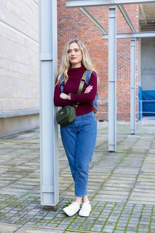 Young woman leaning on column in courtyard wearing maroon turtleneck and backpack