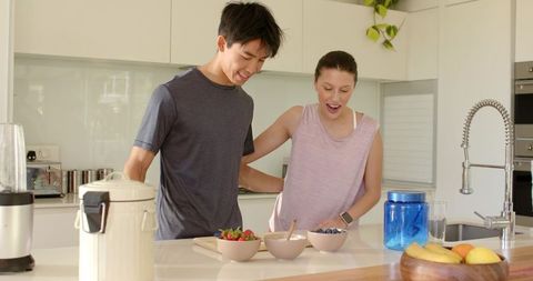 Young couple arranging breakfast bowls on bright modern minimalist kitchen island
