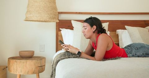 Relaxed Woman Using Smartphone on Bed in Minimalist Bedroom