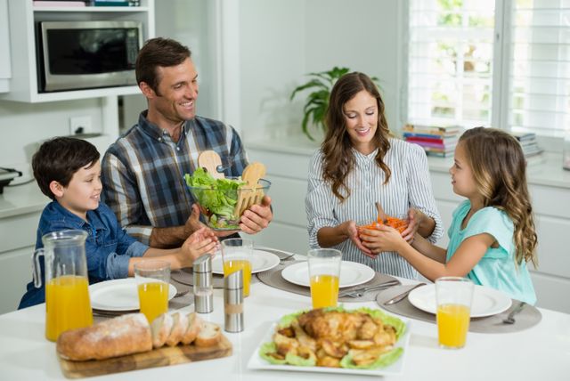 Family gathered around dining table sharing a meal, promoting family bonding and healthy eating. Ideal for use in advertisements, family-oriented content, and articles about family life, nutrition, and home dining.