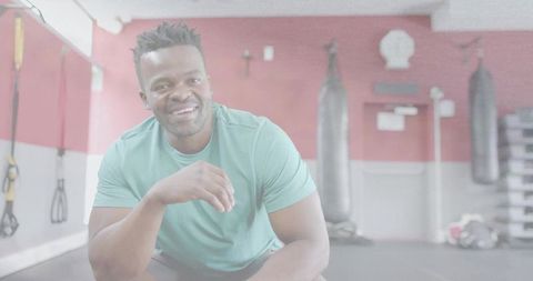 Crouching man smiling while training in gym with punching bags and suspension straps