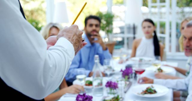 Group of friends are enjoying their meal at an upscale restaurant. Waiter is taking their order while they engage in conversation. Picture can be used for topics related to dining out, restaurant service, social gatherings, hospitality industry, and special occasions.