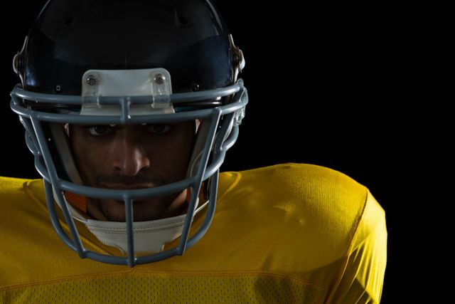 Close-up of an American football player wearing a helmet and yellow jersey, looking determined. Ideal for use in sports promotions, athletic gear advertisements, motivational posters, and articles about football or team sports.