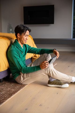 Asian man sitting on floor holding tablet in minimalist modern bedroom with natural light