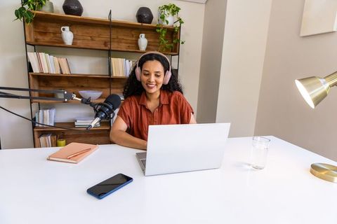 African american woman recording podcast in stylish home office with laptop and microphone