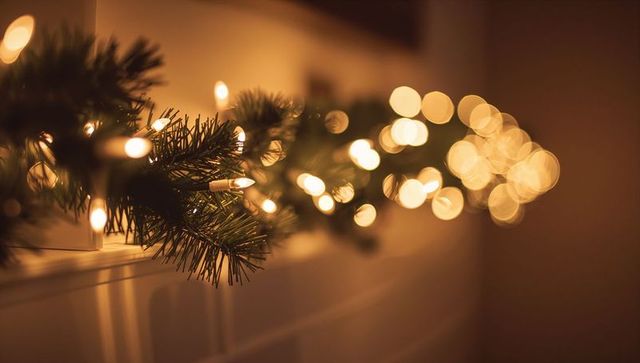Glowing evergreen garland draping mantel with warm white lights and amber bokeh
