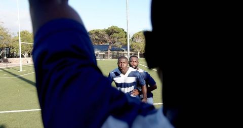 Rugby players running toward camera with dramatic foreground silhouette on green pitch