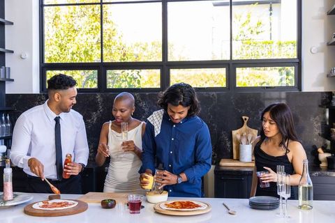 Diverse friends preparing homemade pizzas at sunlit modern kitchen island casual gathering