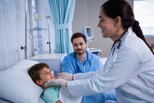 Doctors examining a young patient in a hospital ward. The child is lying in bed while a female doctor checks his throat and a male doctor observes. This image can be used for healthcare, medical, pediatric care, and hospital-related content.