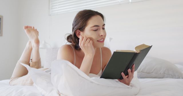 Young woman enjoys quiet time reading on bed, perfect for themes of relaxation, home leisure, self-care, and literature. Ideal for content about home lifestyles, reading habits, and comfortable living spaces.