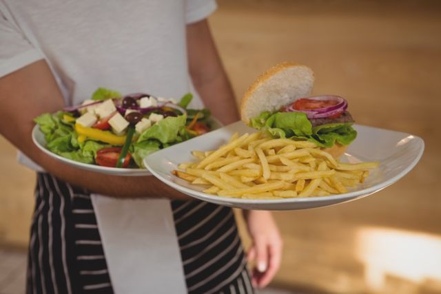Mid section of waiter holding plates with French fries and salad in cafe
