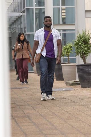 Diverse commuters walking urban corridor carrying messenger bag and coffee by glass facade