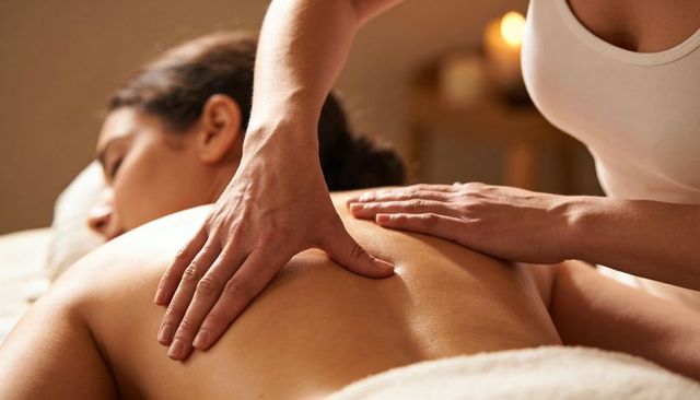 Massage therapist giving relaxing back massage on spa table with candlelight ambience
