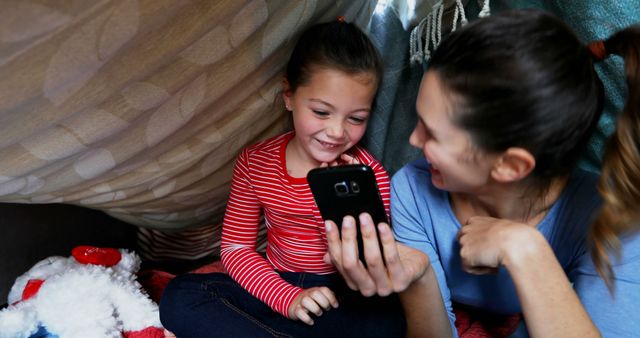 Mother and Daughter Smiling Under Blankets Watching Smartphone - Download Free Stock Images Pikwizard.com
