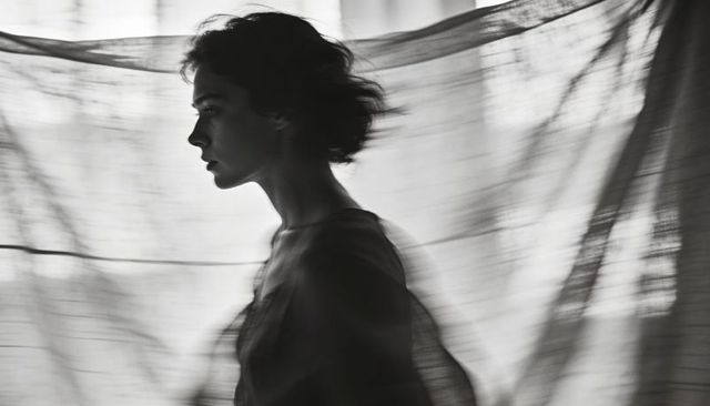 Silhouette woman moving behind sheer curtain in moody black and white cinematic portrait