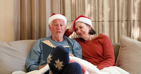 Senior Couple Reading Together with Santa Hats in Cozy Living Room