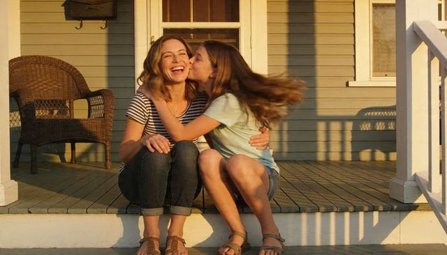 Mother and teen daughter sharing kiss on sunny front porch steps at golden hour