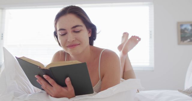 Happy caucasian woman relaxing, lying in bed and reading book. Spending quality time at home concept.