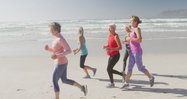 Senior women are jogging together on a beach during the morning. They are dressed in athletic wear and are enjoying the exercise by the ocean. Perfect for promoting healthy lifestyle activities for seniors, group exercise classes, or fitness retreats aimed at older adults.