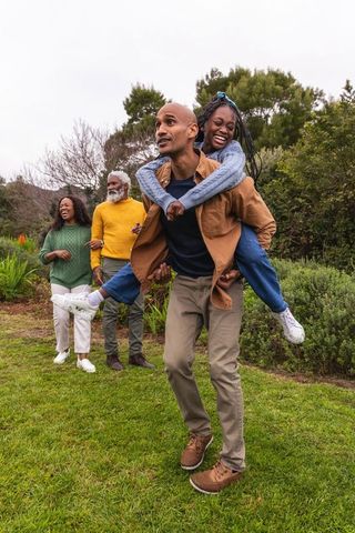 Multigenerational african american family enjoying playful piggyback walk in park garden