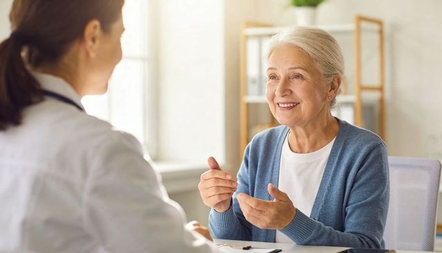 Senior woman smiling and consulting with doctor in bright clinic, patient-centered care