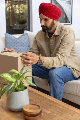 Man in red turban unboxing package on living room sofa