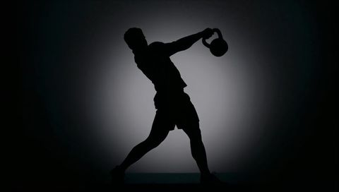 Backlit male silhouette performing explosive kettlebell swing under halo spotlight