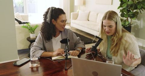 Two women hosting a podcast at home with microphones and laptop