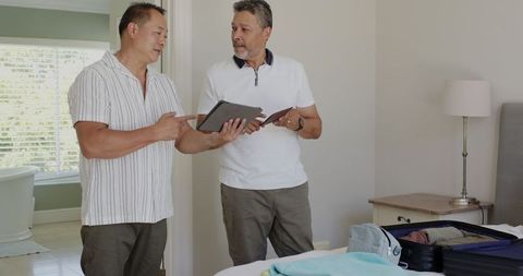 Two senior men packing suitcase at home for travel
