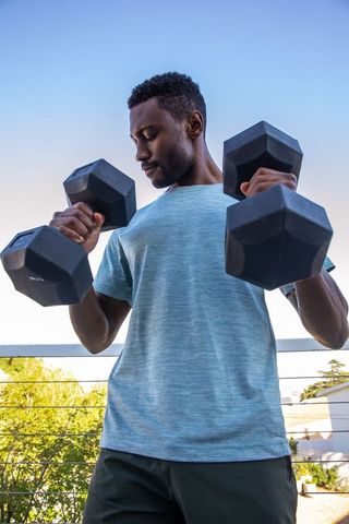Determined Man Lifting Dumbbells Outdoors for Strength and Wellness