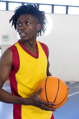 Basketball Player Wearing Yellow Jersey Holding Ball on Indoor Court