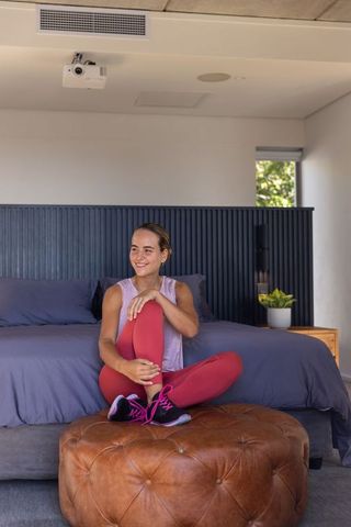 Young woman relaxing on tufted leather ottoman in modern bedroom after home workout