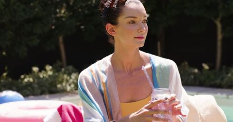 Woman Enjoying Refreshing Drink by Backyard Pool in Summer Attire