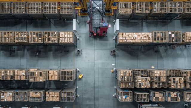 Automated red stacker operating in high-bay warehouse with workers walking central aisle