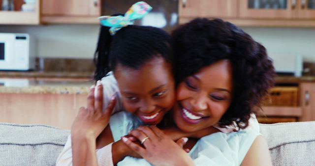African American mother and teenage daughter share a warm embrace, smiling with affection in a cozy home setting. Their close bond and joyful interaction convey a sense of love and family unity.