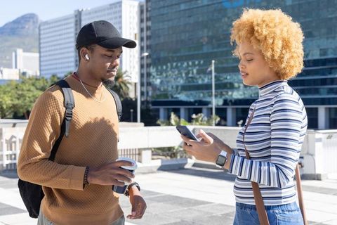 African american friends sharing smartphone on urban plaza holding coffee and earbuds