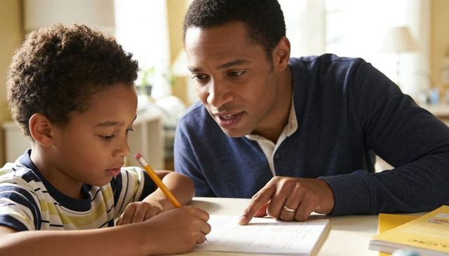 Father guiding son doing homework at home helping with writing focused learning