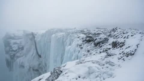 Drone panning over frozen cliff and glacier icefall on foggy Arctic coast showing crevasse