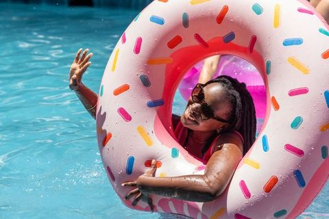 Smiling woman floating on pink sprinkle donut inflatable, wearing sunglasses, summer pool
