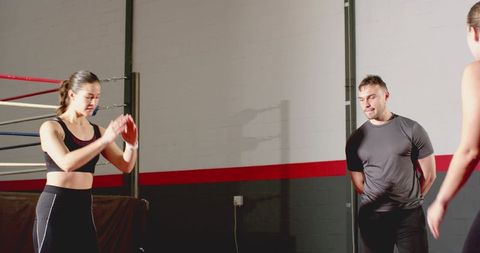 Coach observing female boxer training with red medicine ball near boxing ring ropes