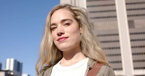 Confident young woman smiling in urban sunlight near office tower